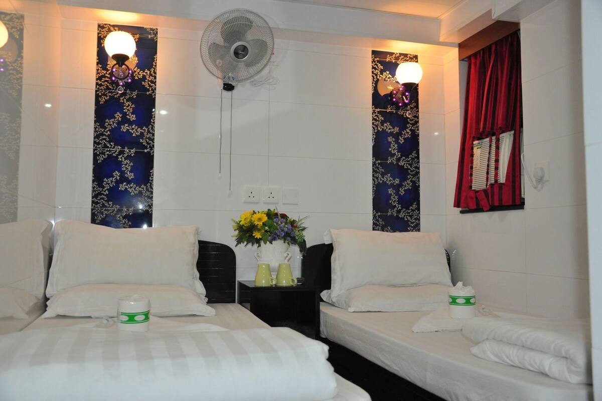 A hotel room with two beds, a nightstand with a vase of flowers, and wall-mounted fans.