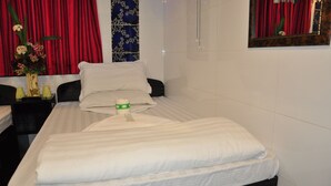 Una cama bien hecha con sábanas blancas, un florero con flores y una mesita de noche con una lámpara y una botella.