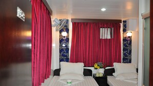 Habitación de hotel con dos camas, cortinas rojas, ventilador de techo e iluminación montada en la pared.