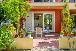 Un patio con mobiliario exterior, plantas en macetas y vista al interior.
