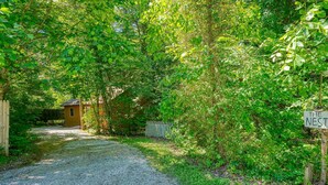 A gravel path leading to a wooden structure labeled "The Nest" surrounded by dense greenery. - The Nest at Hiding Place Cabins (Logan)