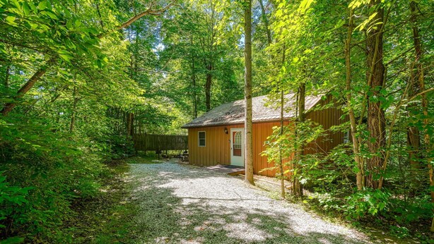 A rustic cabin surrounded by dense forest, with a gravel path leading to the entrance. - The Nest at Hiding Place Cabins (Logan)