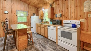 A wooden-paneled kitchen with a dining table, chairs, a refrigerator, a microwave, an oven, and a clock. - The Nest at Hiding Place Cabins (Logan)