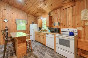 A wooden cabin kitchen with a dining table, chairs, a refrigerator, a microwave, a stove, and a sink. - The Nest at Hiding Place Cabins (Logan)