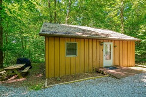 A small wooden cabin with a door and window, surrounded by a forest. - The Nest at Hiding Place Cabins (Logan)