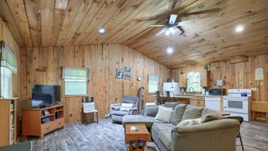 A cozy cabin interior with a wooden interior, a television, a sofa, a chair, and a kitchenette. - The Nest at Hiding Place Cabins (Logan)