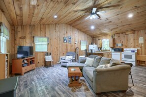 A cozy cabin interior with a wooden interior, a television, a sofa, a chair, and a kitchenette.