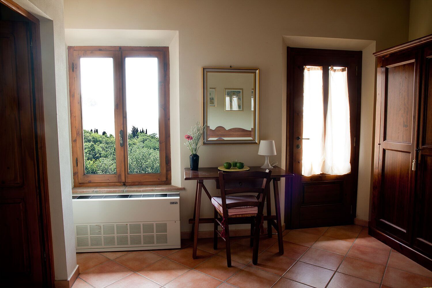 Une pièce avec une fenêtre, un radiateur, une table avec une lampe et une chaise.