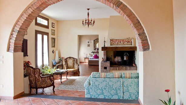 A living room with a brick archway, a fireplace, a chandelier, and a patterned sofa. - Podere l'Ulivo: typical Tuscan Villa of 400 meters with a large swimming pool (San Mignato Pisa)