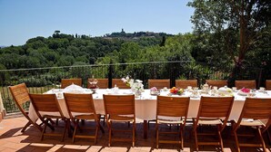 An outdoor dining area with a table set for a meal, surrounded by chairs, and overlooking a scenic view of a hill with trees and buildings. - Podere l'Ulivo: typical Tuscan Villa of 400 meters with a large swimming pool (San Mignato Pisa)