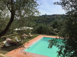 Una piscina rectangular con borde de azulejos, rodeada por una terraza de madera y dos sillas reclinables.