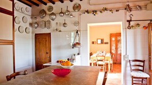 A dining area with a table set for four, a kitchen with hanging pots and pans, and a wooden door. - Podere l'Ulivo: typical Tuscan Villa of 400 meters with a large swimming pool (San Mignato Pisa)