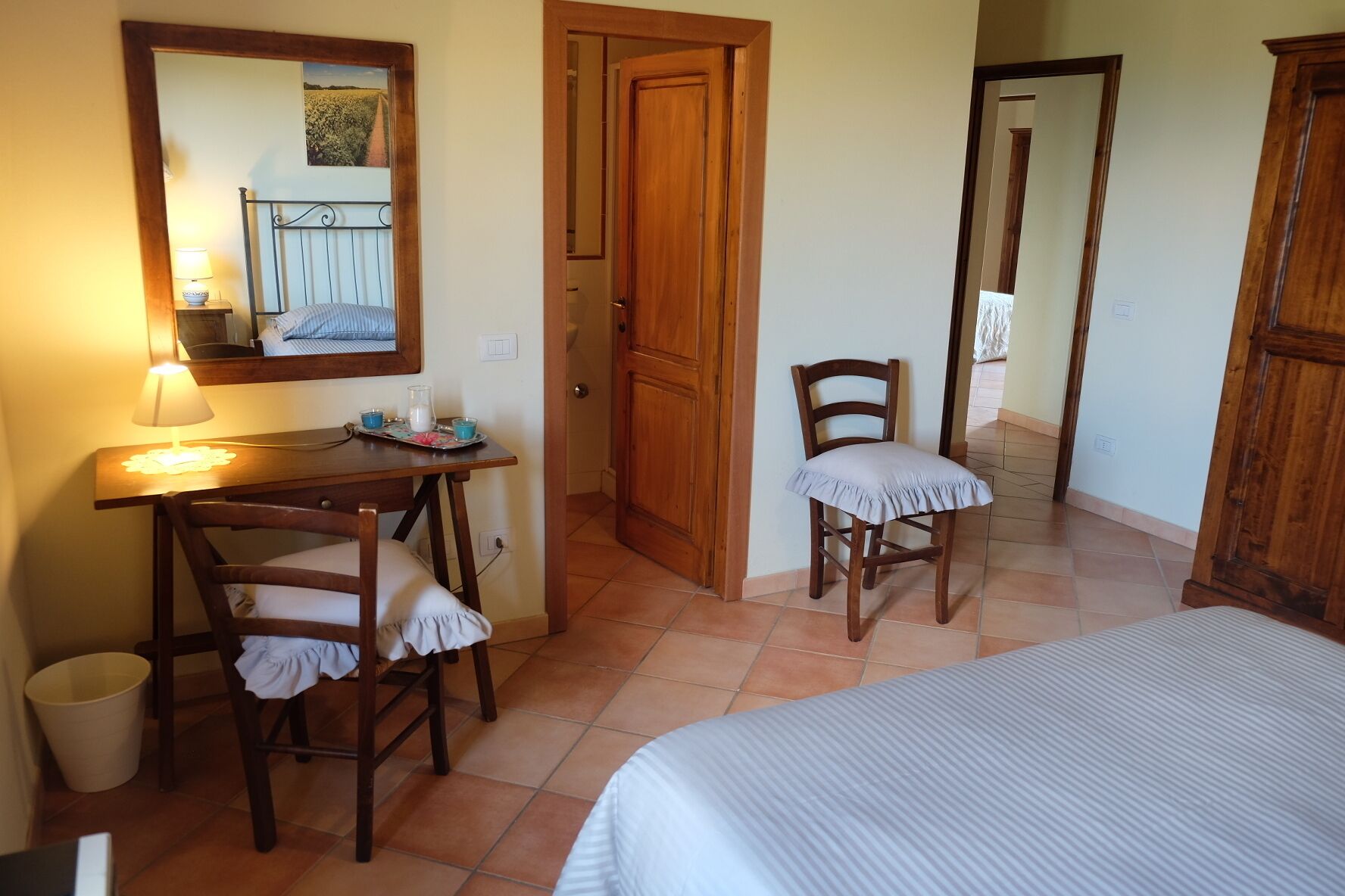 A bedroom with a bed, a desk with a chair, a wooden wardrobe, and a door leading to another room.