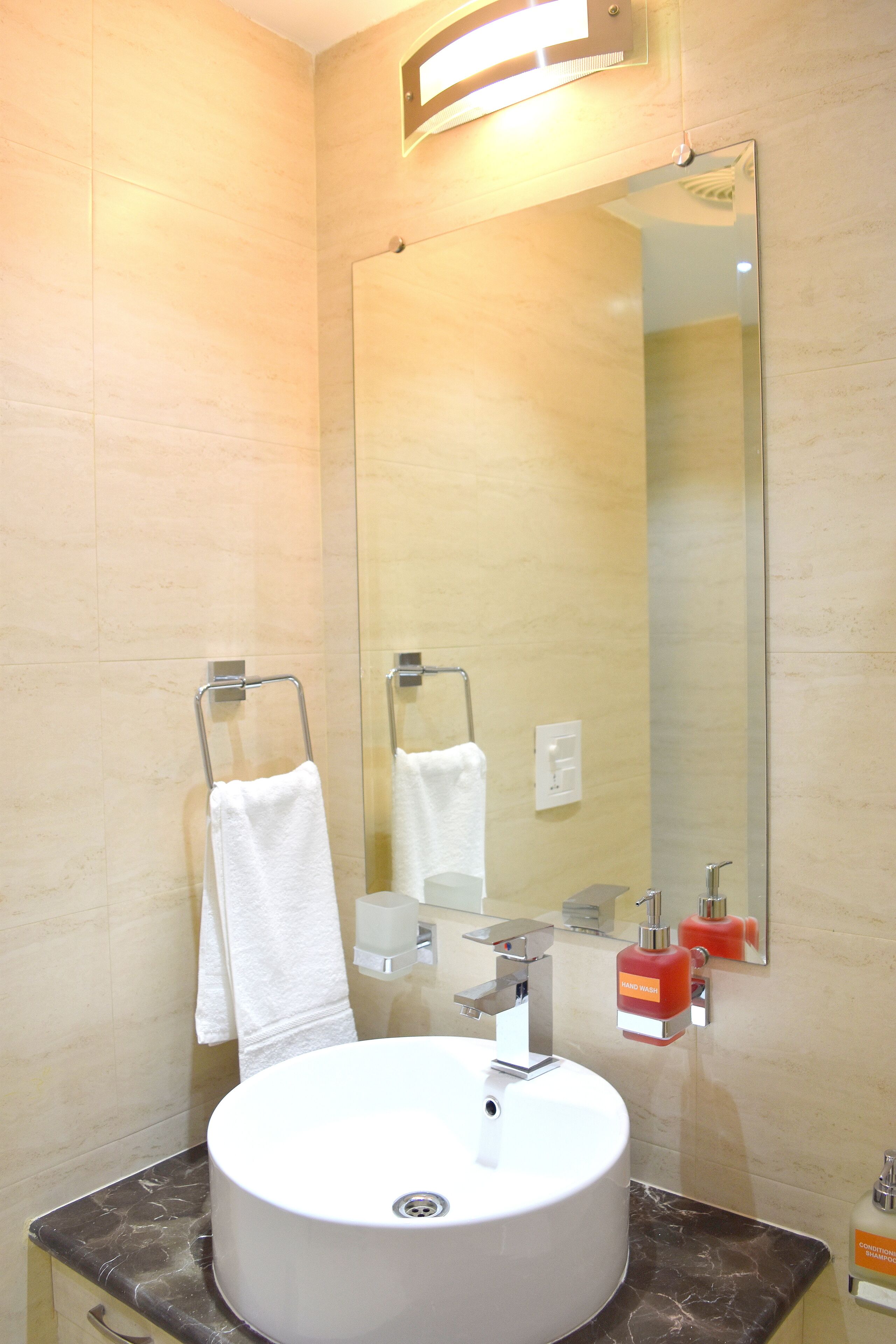 A bathroom with a round sink, a towel rack, a mirror, and a soap dispenser.