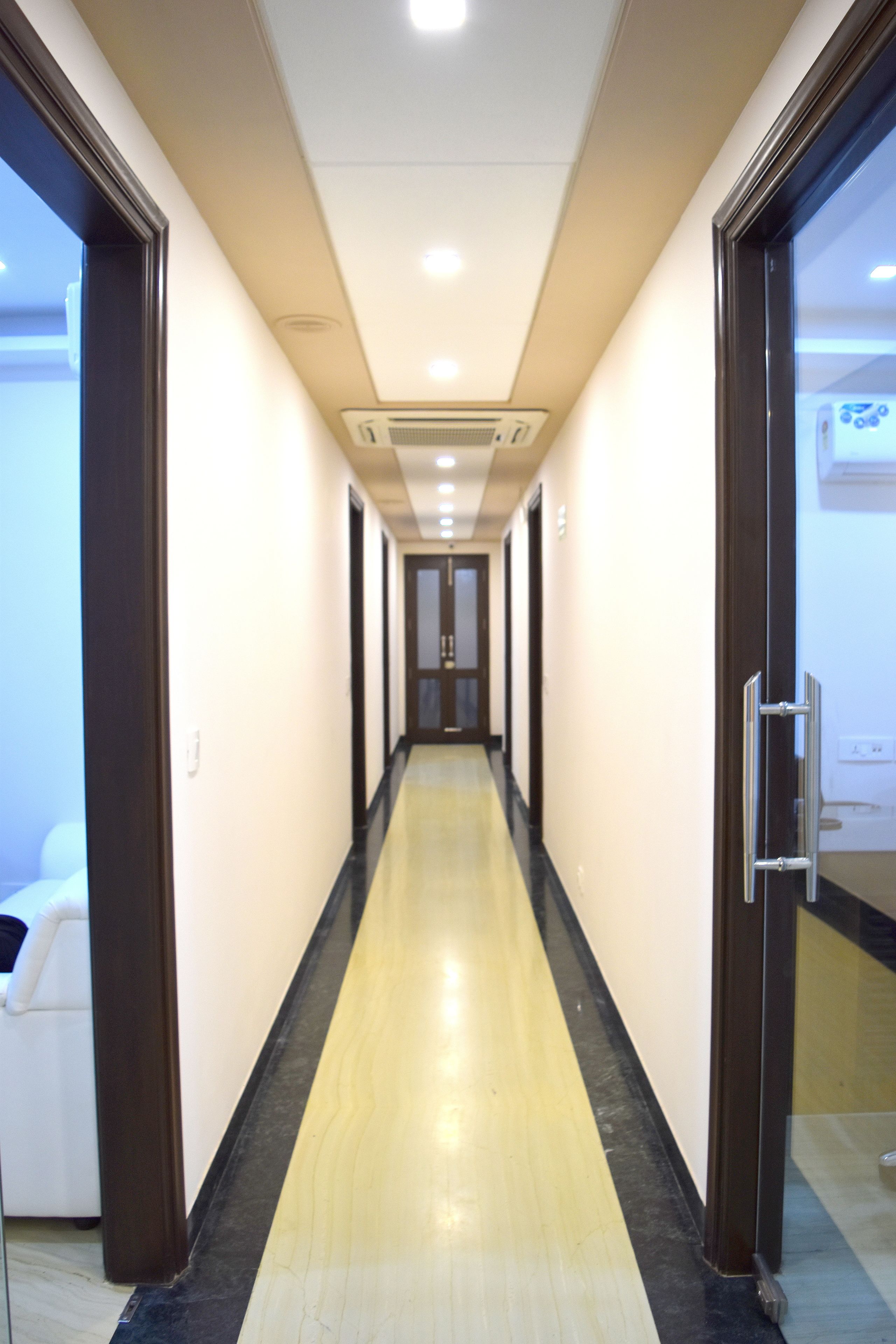 A long, narrow hallway with a black and yellow floor, white walls, and doors on both sides.