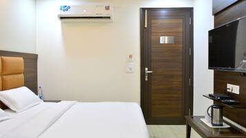 Habitación de hotel con una cama, una puerta de madera, un televisor y una mesita con un hervidor.