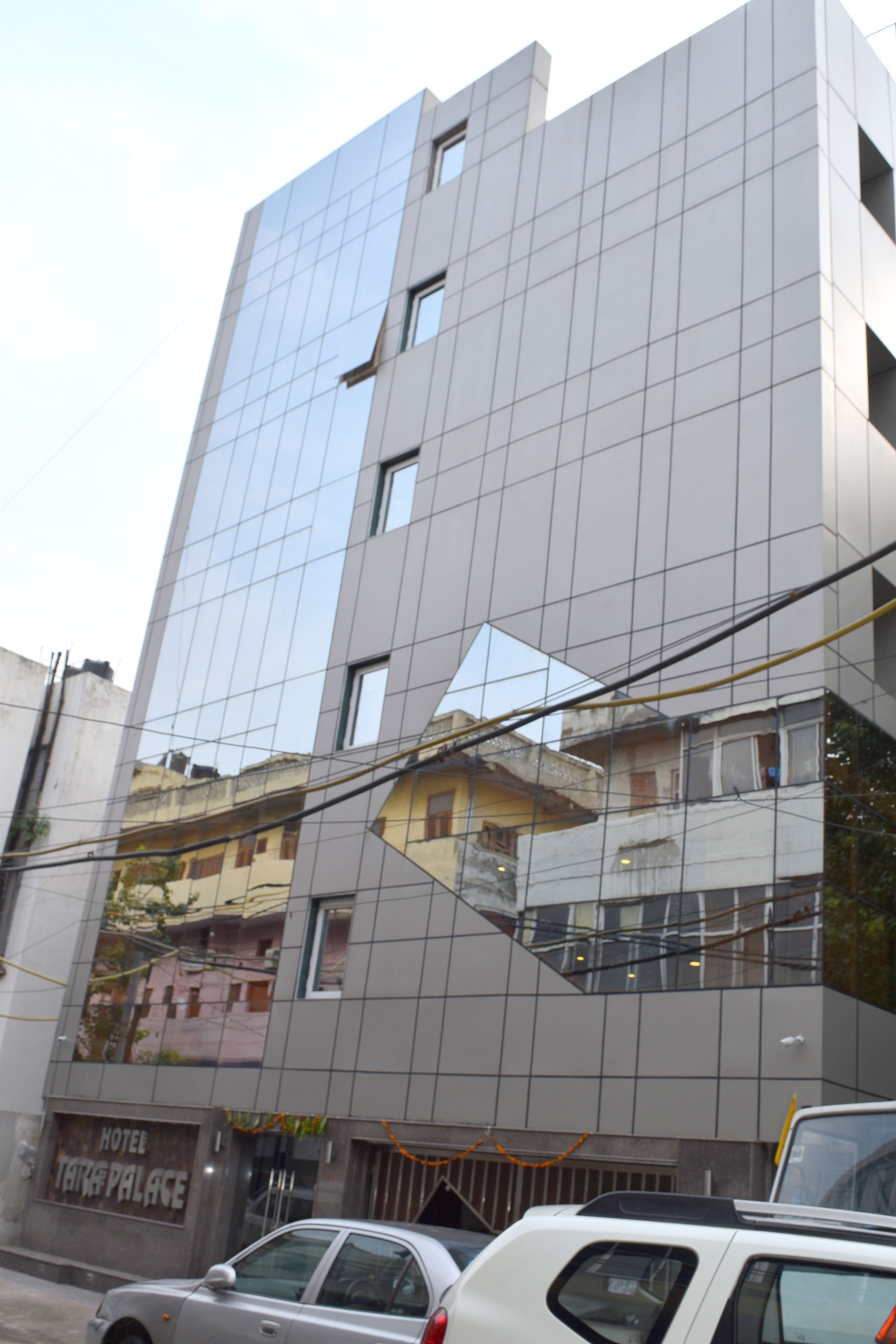 Un edificio moderno con fachada de vidrio, un letrero visible que dice 'Hotel Tara Palace' y automóviles estacionados al frente.