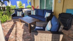 Ein überdachter Patio-Bereich mit Korbmöbeln, einem Couchtisch und einem Grill.