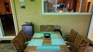 Eine Terrasse im Freien mit einem Holztisch und Stühlen, einem Kühlschrank und einer Wanduhr.