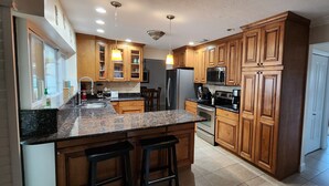 Eine Küche mit Holzausstattung, Granit Arbeitsplatten, einem Edelstahl-Kühlschrank, einer Mikrowelle und einem Herd.