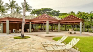 A covered outdoor area with lounge chairs and tables, surrounded by palm trees and greenery. - Private and Quiet, Luxury Family-Friendly unit in Fairways at Mauna Lani (Waimea)