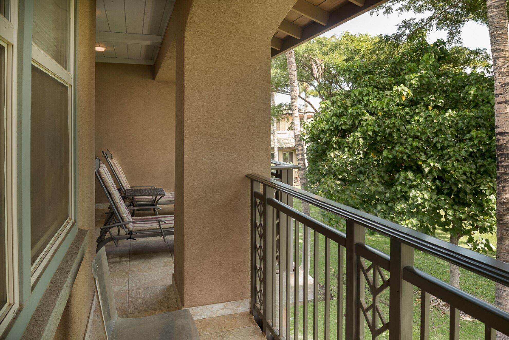 A balcony with a view of a lush green tree and a building in the background.