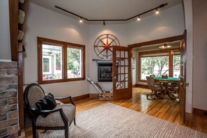 A spacious room with a fireplace, a large window, a wooden door, and a billiards table. - Whitefish Downtown Classic home! (Whitefish)