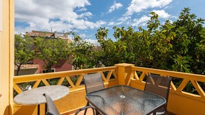 Een balkon met gele leuning, een glazen tafel en twee stoelen.