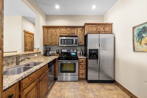 Une cuisine dotée de plans de travail en granit, d’appareils électroménagers en acier inoxydable, d’armoires en bois et d’un revêtement de sol en carrelage.