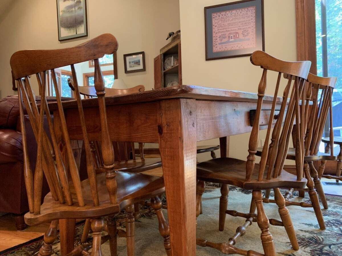 A wooden dining table with four chairs, a framed picture on the wall, and a window with natural light.