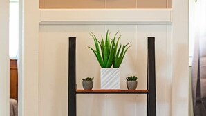 A wooden ladder shelf with a blue patterned cushion, a white vase with green plants, and a small container. - Hale Leilani - Adventure Awaits (Hilo)