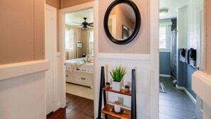 A hallway with a bed, a mirror, and a shelf with plants. - Hale Leilani - Adventure Awaits (Hilo)