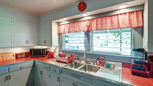 A kitchen with a red and white checkered window valance, a microwave, a sink, and a blender. - Hale Leilani - Adventure Awaits (Hilo)