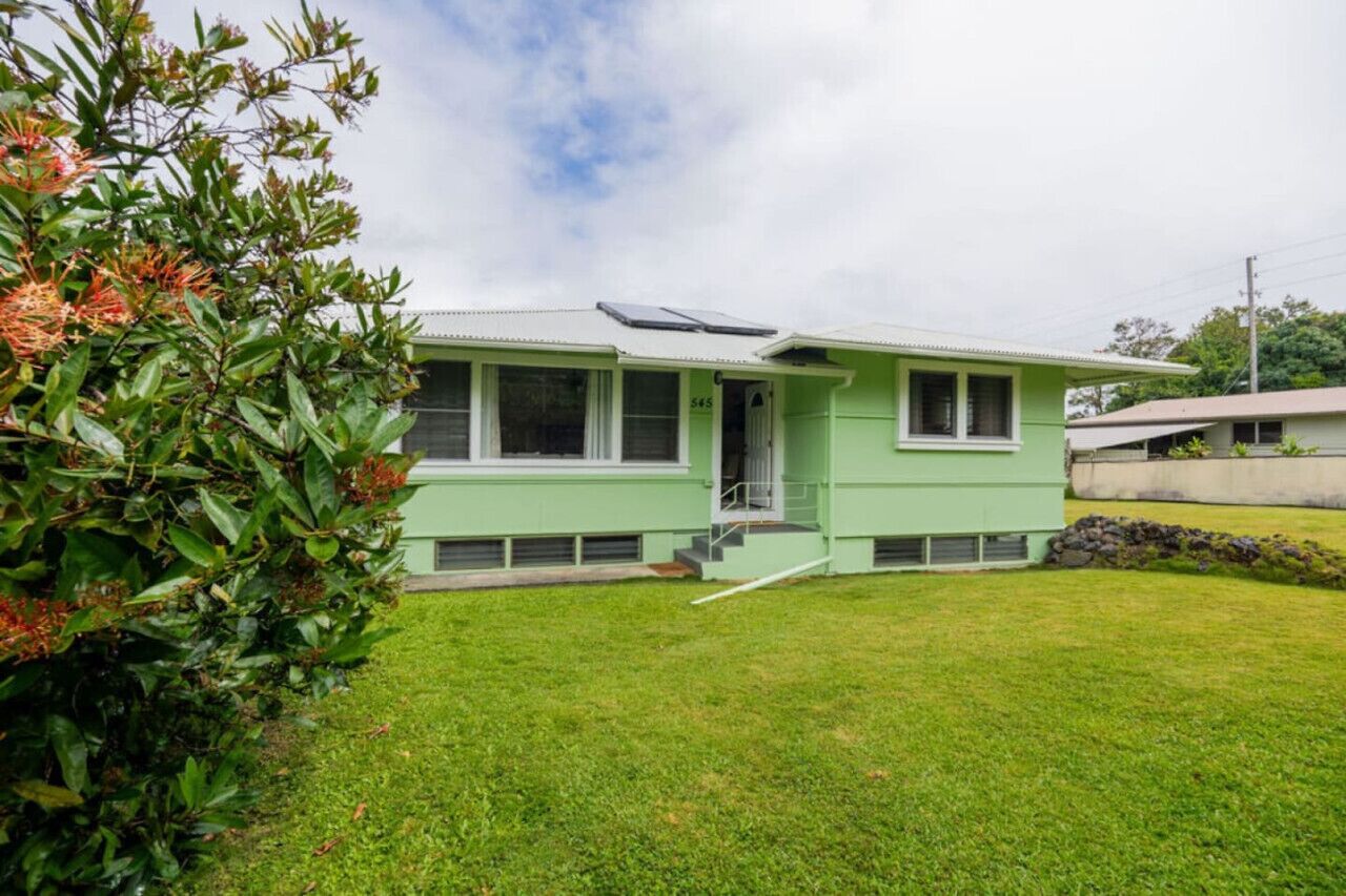 A single-story house with a green exterior, a visible number '545' on the side, and a small front yard with grass and a bush.
