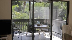 A balcony with a table and chairs, a TV, and a view of greenery. - Captiva home- steps from the beach, pool, restaurants and boat dock (Captiva)
