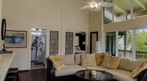 A living room with a sofa, a glass coffee table, and a ceiling fan.