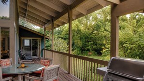 Um deck ao ar livre com churrasqueira, uma mesa com cadeiras e vista para um jardim exuberante.