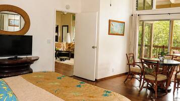 A bedroom with a bed, a television, a ceiling fan, a dining area with chairs and a table, and a window with a view.