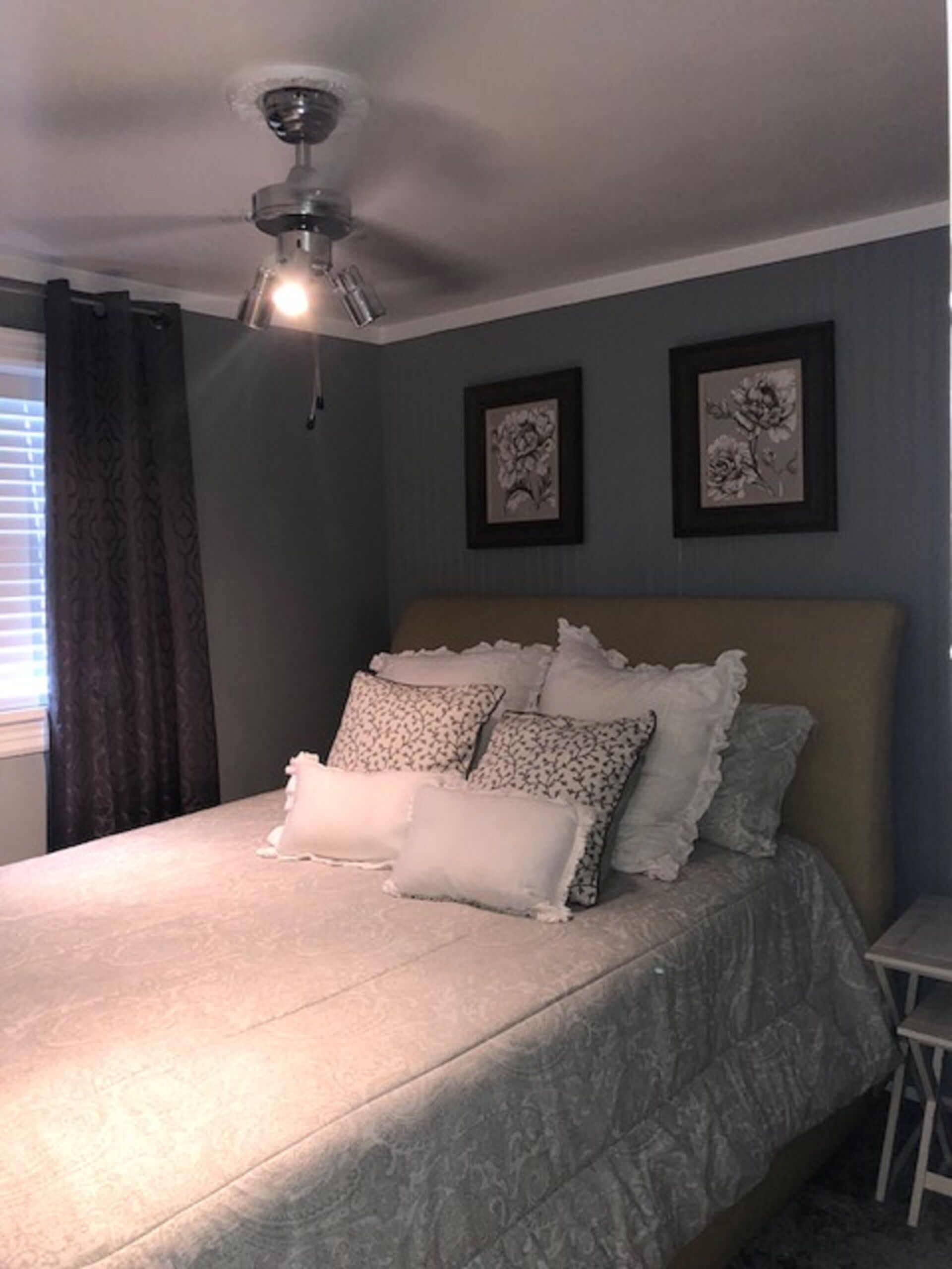 Ein Schlafzimmer mit einem Bett, einem Deckenventilator und zwei gerahmten Blumenbildern an der Wand.