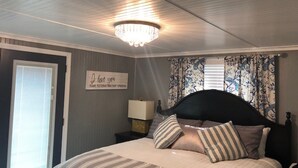 A bedroom with a bed, a nightstand, a lamp, a chandelier, and a decorative sign on the wall. - Walk to Downtown/The Landing! Beautiful cottage, cozy private hot tub! (Branson)