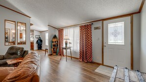 A spacious living room with a brown leather couch, wooden flooring, a small table with a lamp, and a door with a decorative window. - Fisherman's Dream! Directly on the beautiful Watauga River!  Walk in access! (Elizabethton)