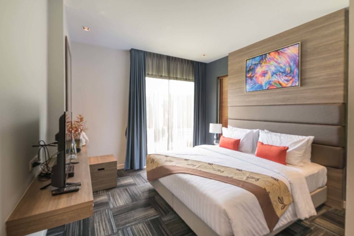 Een hotelkamer met een groot bed, een bureau met een computer, een televisie en een raam met gordijnen.