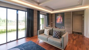 Un salon moderne avec un canapé gris, une grande fenêtre et une vue sur l’extérieur.