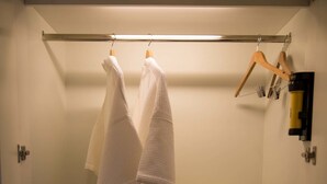 Une salle de bain avec un porte-serviettes sur lequel sont posées deux serviettes blanches, un meuble blanc contenant des articles de toilette et une étagère avec des serviettes pliées et des chaussons.
