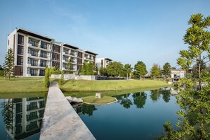 Un bâtiment moderne doté de nombreux balcons, d’un élément décoratif aquatique réfléchissant et entouré de verdure.