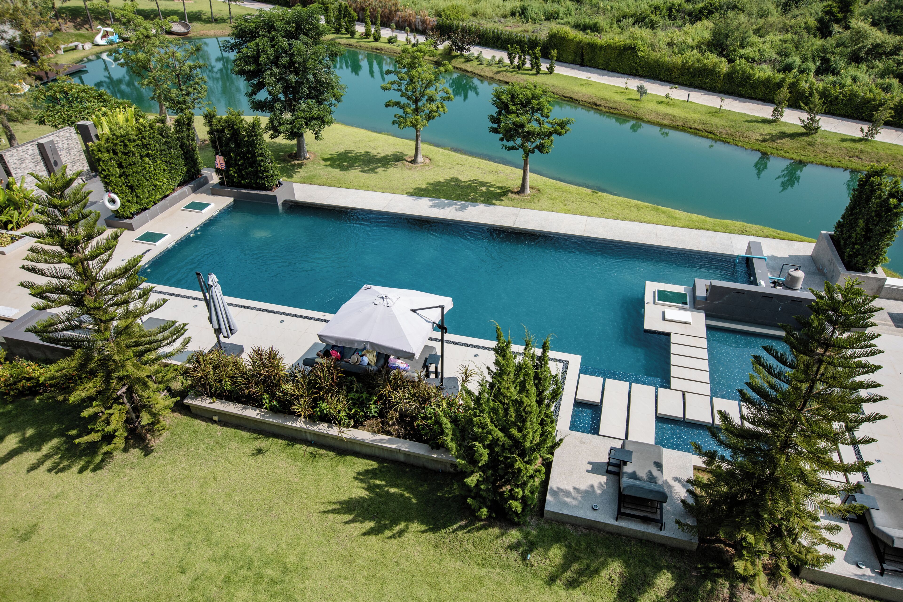 A large rectangular swimming pool with a surrounding deck, a smaller circular pond, and a landscaped garden with trees and shrubs.