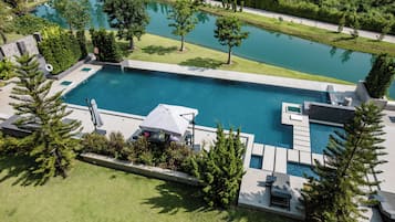 A large rectangular swimming pool with a surrounding deck, a smaller circular pond, and a landscaped garden with trees and shrubs.