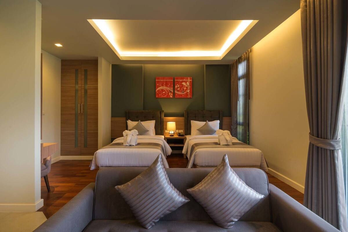 Een hotelkamer met twee bedden, een slaapbank, een kledingkast en een plafondlamp.
