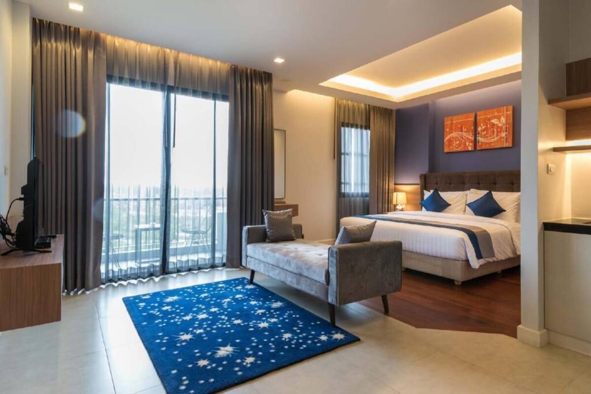 Een moderne hotelkamer met een bed, een slaapbank, een bureau en een groot raam met gordijnen.