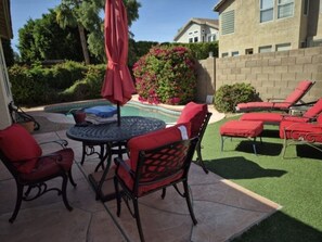 Un patio al aire libre con una mesa redonda y sillas, una piscina y sillones rojas para tomar el sol.